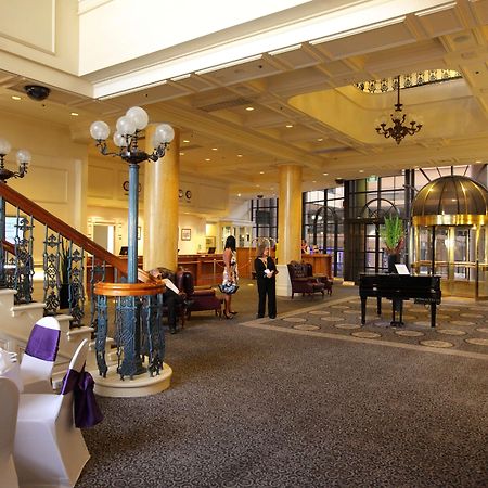 Hotel Stamford Grand Adelaide Glenelg Interior foto The photo shows a luxurious interior of a hotel or a restaurant lobby. There is an elegant staircase with ornate railings leading to an upper level. The space features high ceilings with decorative chandeliers and ample natural light coming through l