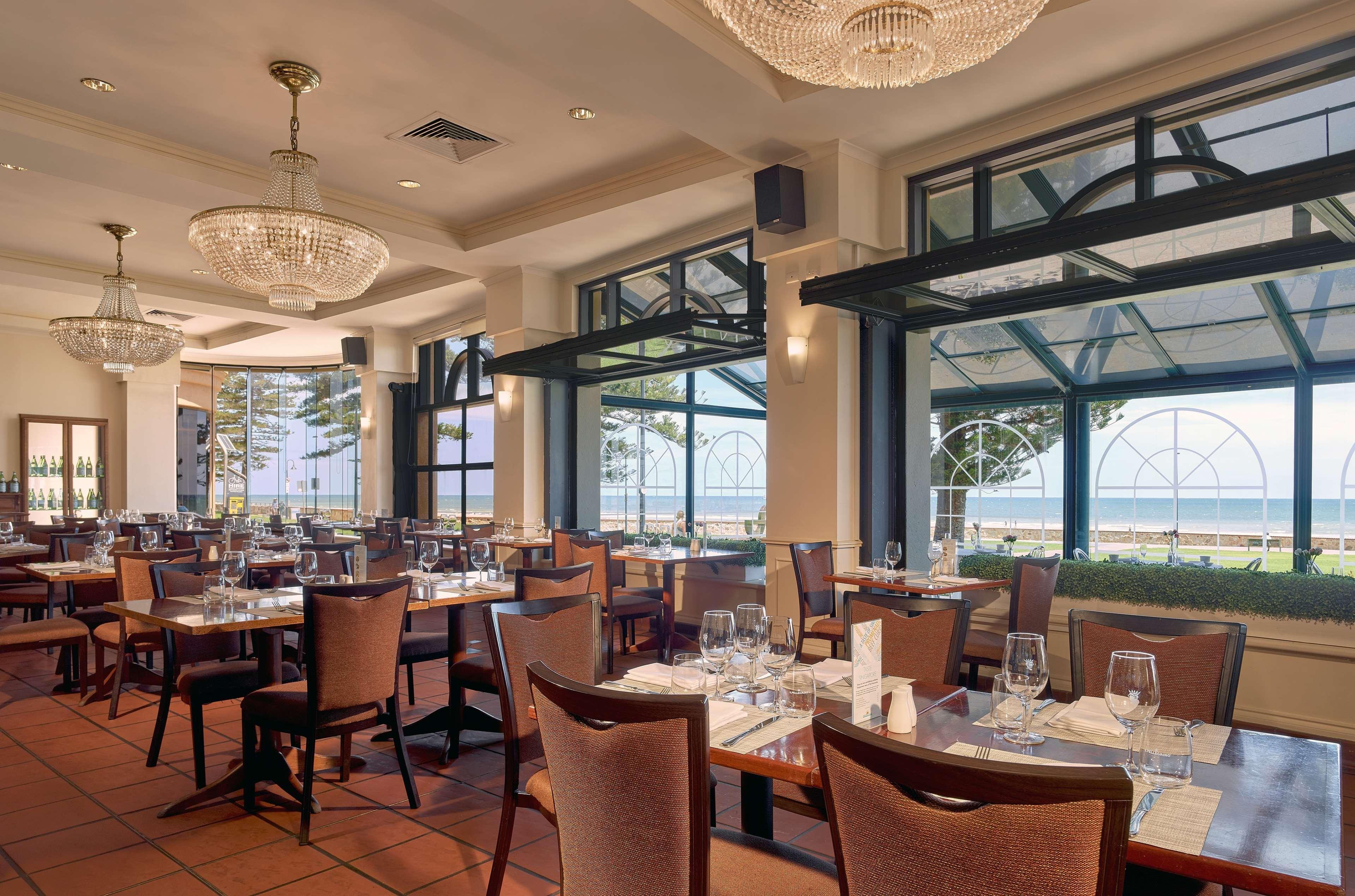 Hotel Stamford Grand Adelaide Glenelg Exterior foto The photo shows the interior of a restaurant. It features several wooden tables set with glasses and utensils, suggesting it's ready for diners. The decor includes elegant chandeliers hanging from the ceiling, adding a touch of sophistication. Large 