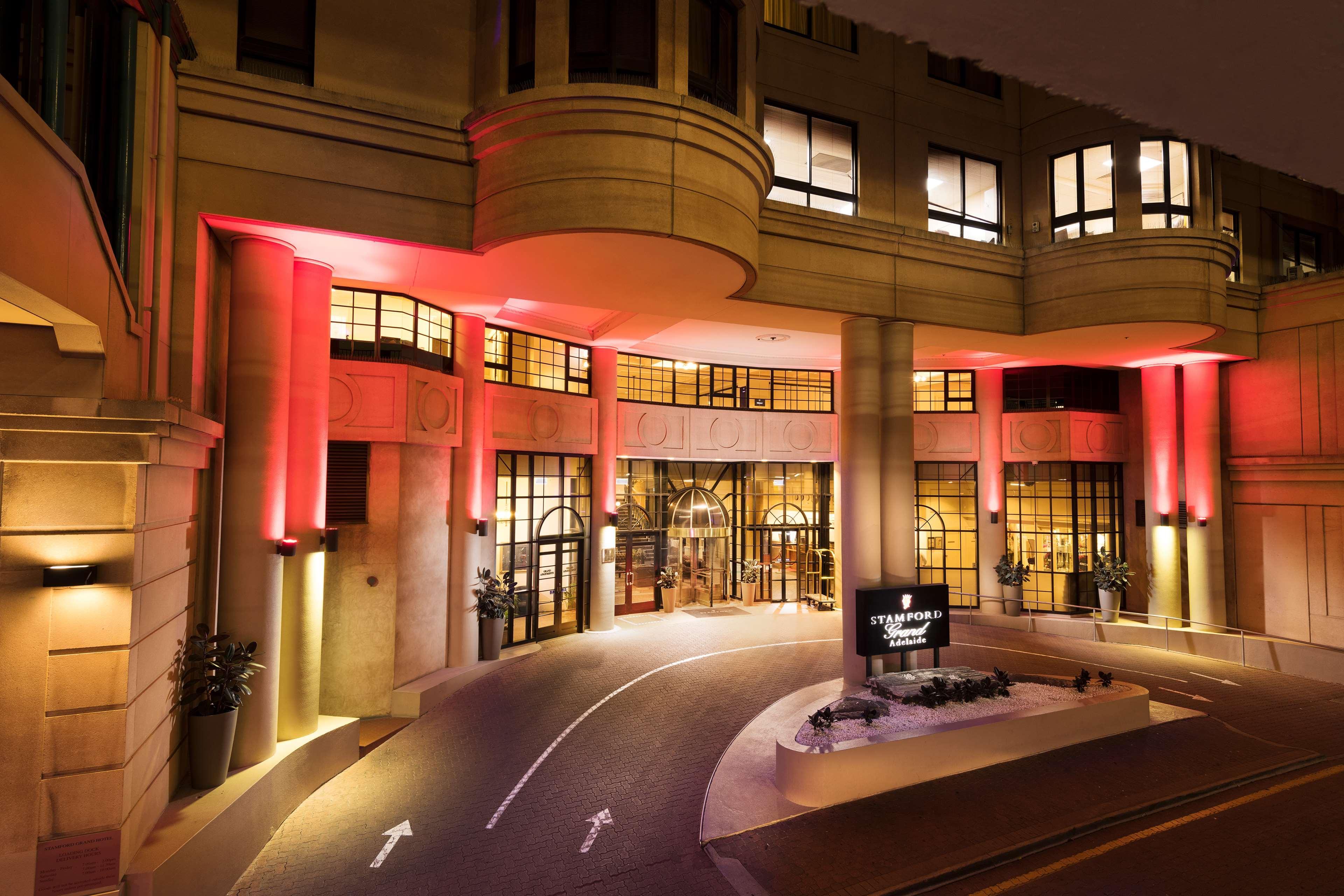 Hotel Stamford Grand Adelaide Glenelg Exterior foto The photo shows the entrance of a hotel or luxury building at night. The façade features a modern architectural style with large windows and an elegant entrance. The area is illuminated with red lighting, creating an inviting atmosphere. There appear