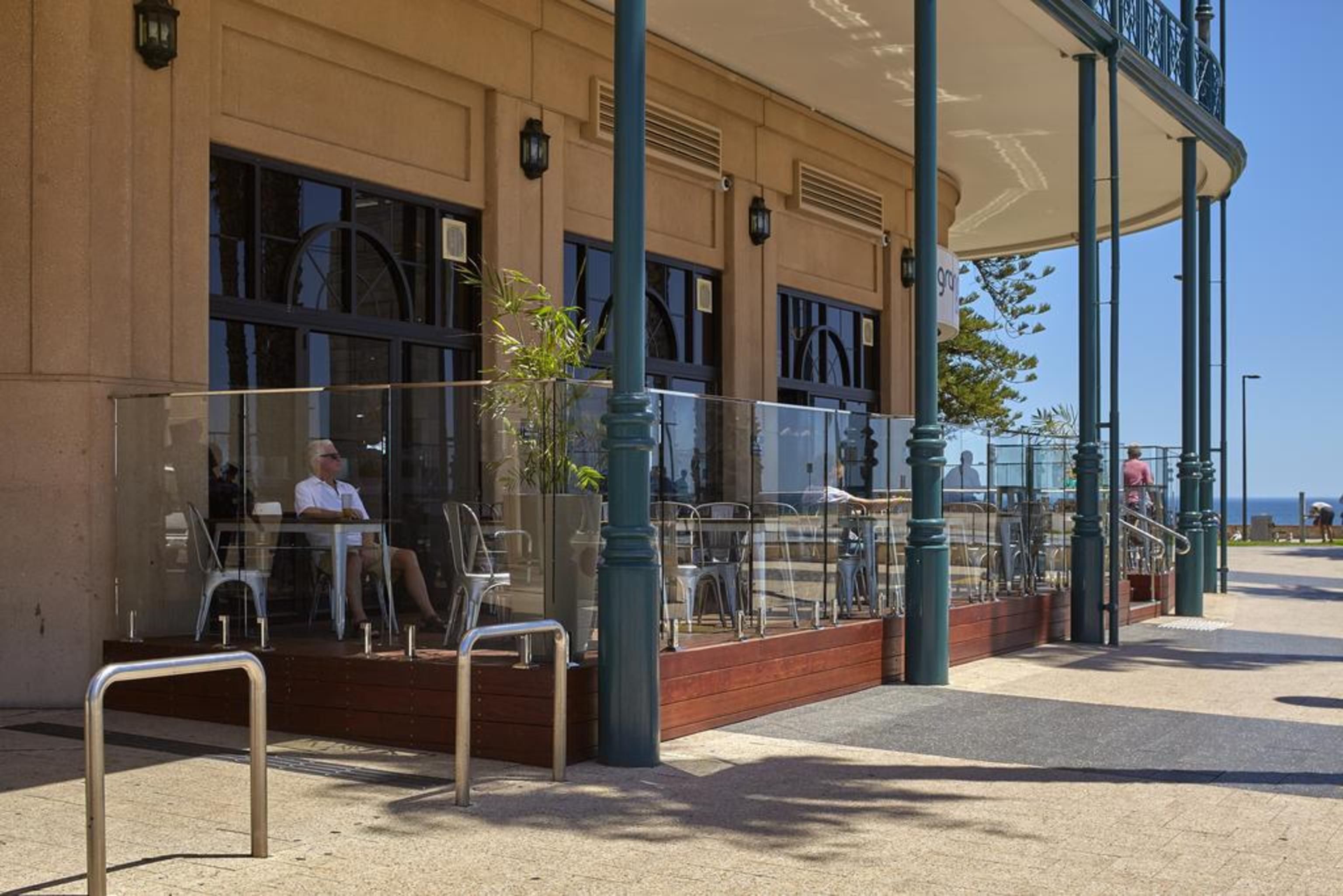 Hotel Stamford Grand Adelaide Glenelg Exterior foto The photo shows the exterior of a cafe or restaurant with a large outdoor seating area. There are glass barriers around the seating, providing a view of the outside while maintaining a sense of enclosure. The building has a modern architectural style