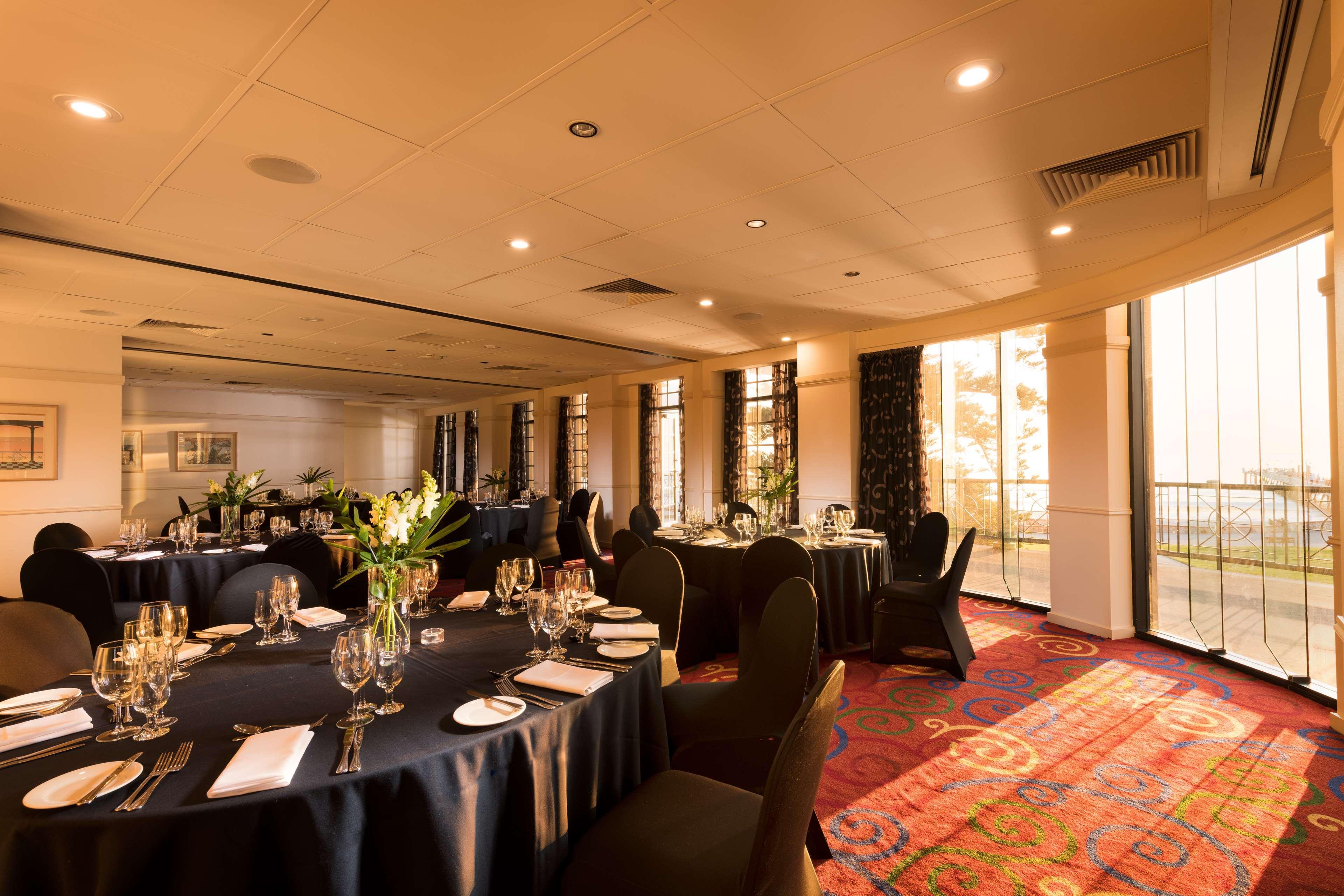 Hotel Stamford Grand Adelaide Glenelg Exterior foto The photo shows a well-decorated event space or dining area. There are several round tables draped in dark tablecloths, each set with elegant dinnerware, including glasses and cutlery. The room features large windows that allow natural light to flood